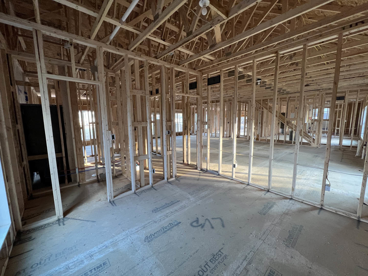 Exposed wood framing and beams with unfinished concrete floor, partially constructed ceiling, and hanging light bulb in a residential interior.