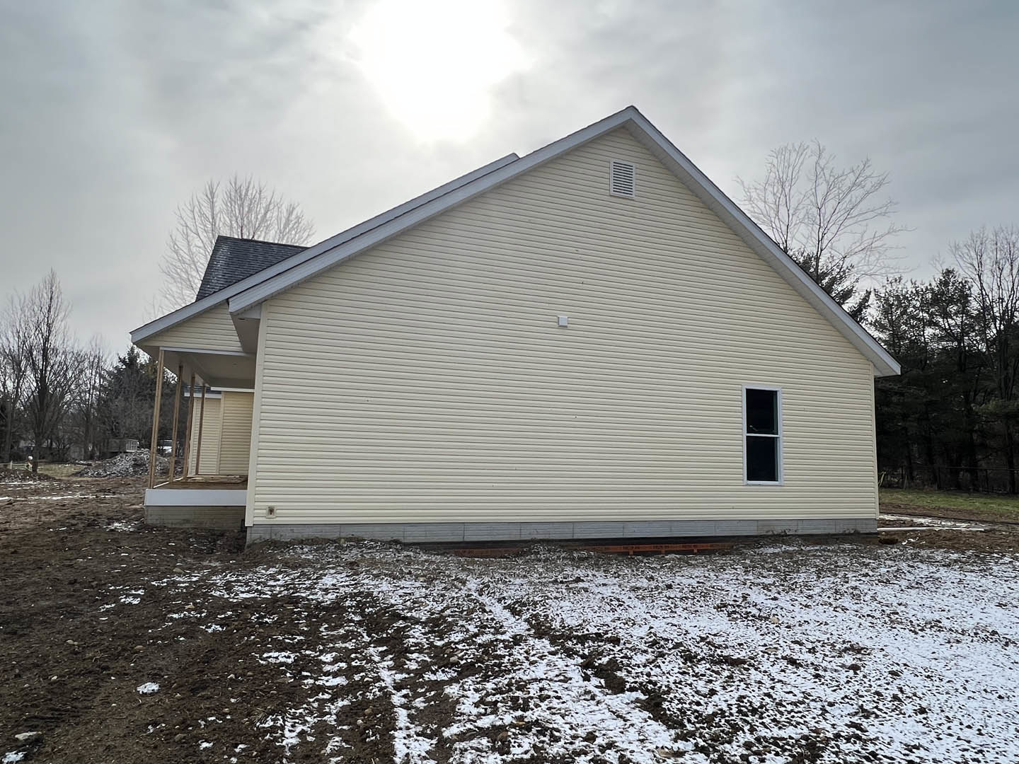Two-story home with gray siding, white-framed windows, and gabled roof, surrounded by snow-covered ground and bare trees under a cloudy winter sky