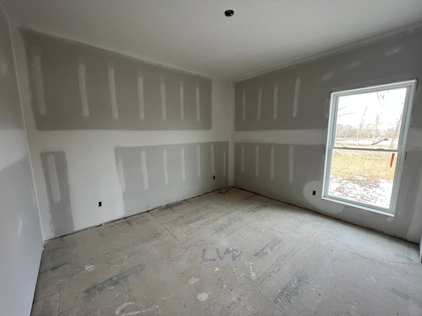 Room with smooth white plaster walls, large window letting in natural light, concrete flooring, and simple ceiling detailing
