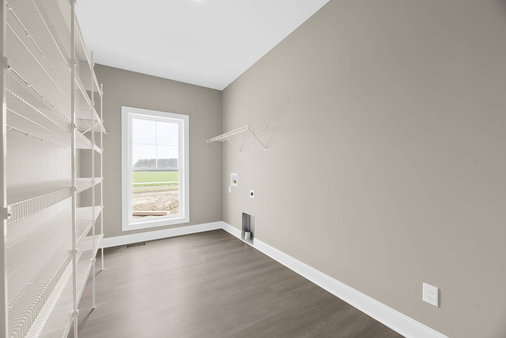Wood flooring with white baseboards, built-in white shelves, plaster walls, and a window overlooking a grassy field