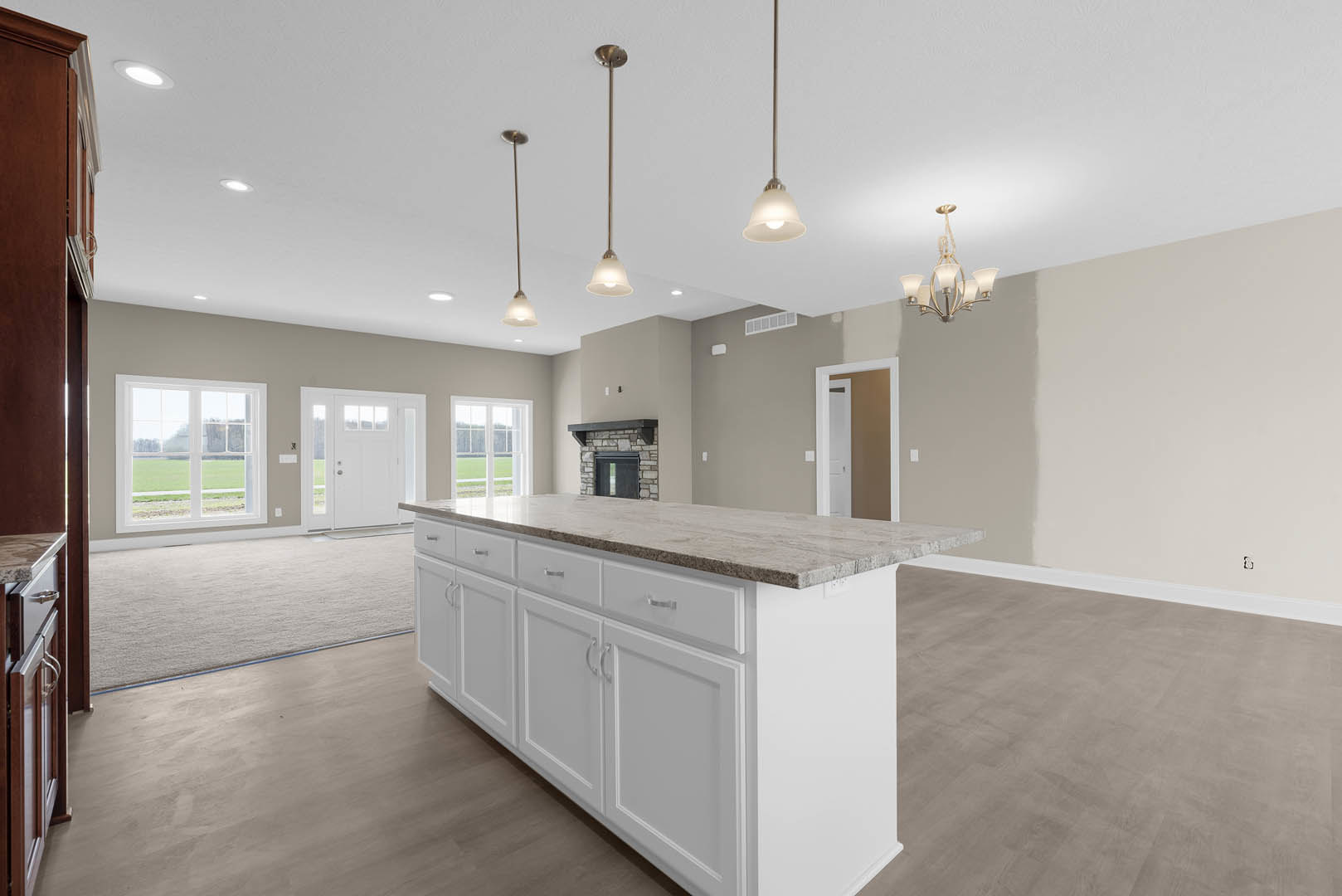 White kitchen island with tile countertop, white cabinetry, stainless sink, and chandelier overhead; window and door with glass panes reveal grassy field outside; fireplace visible