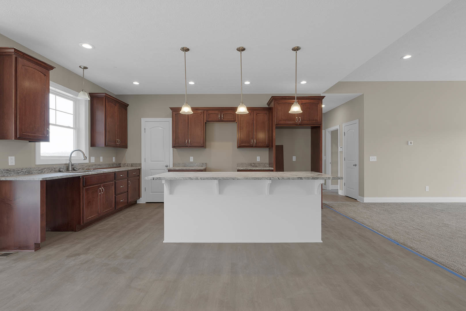 Modern kitchen featuring a central island with stone countertop, white cabinetry with silver handles, tile flooring, stainless steel faucet, pendant light fixture, and white doors