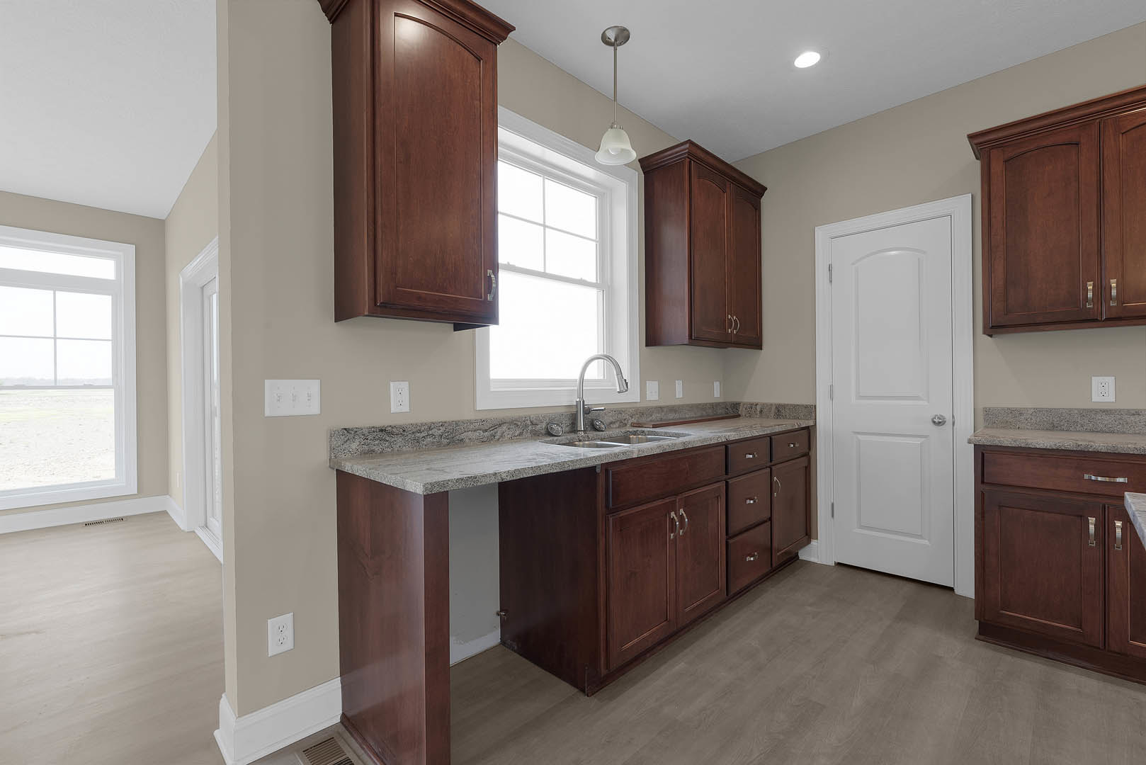 Kitchen with dark wood cabinets, white door with silver handle, multi-pane window, and light-colored countertops