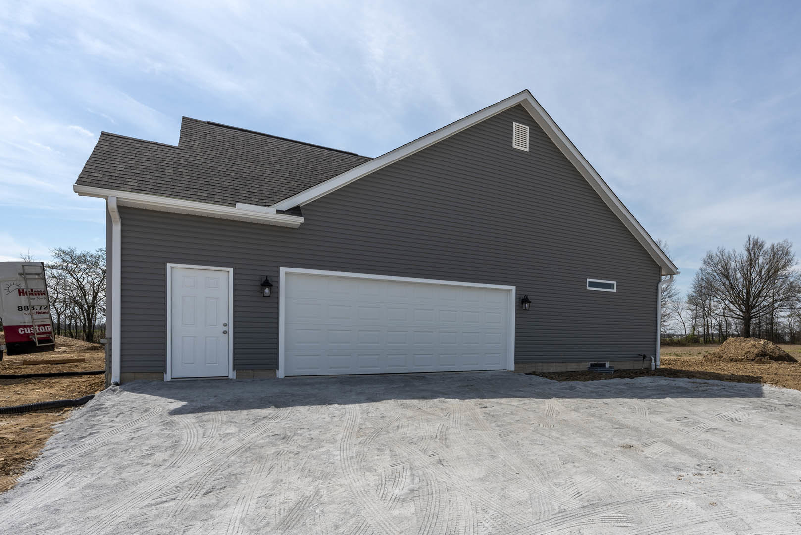 White garage door with silver handles set in light siding, adjacent to a leafless tree and a white entry door; cloudy sky overhead.