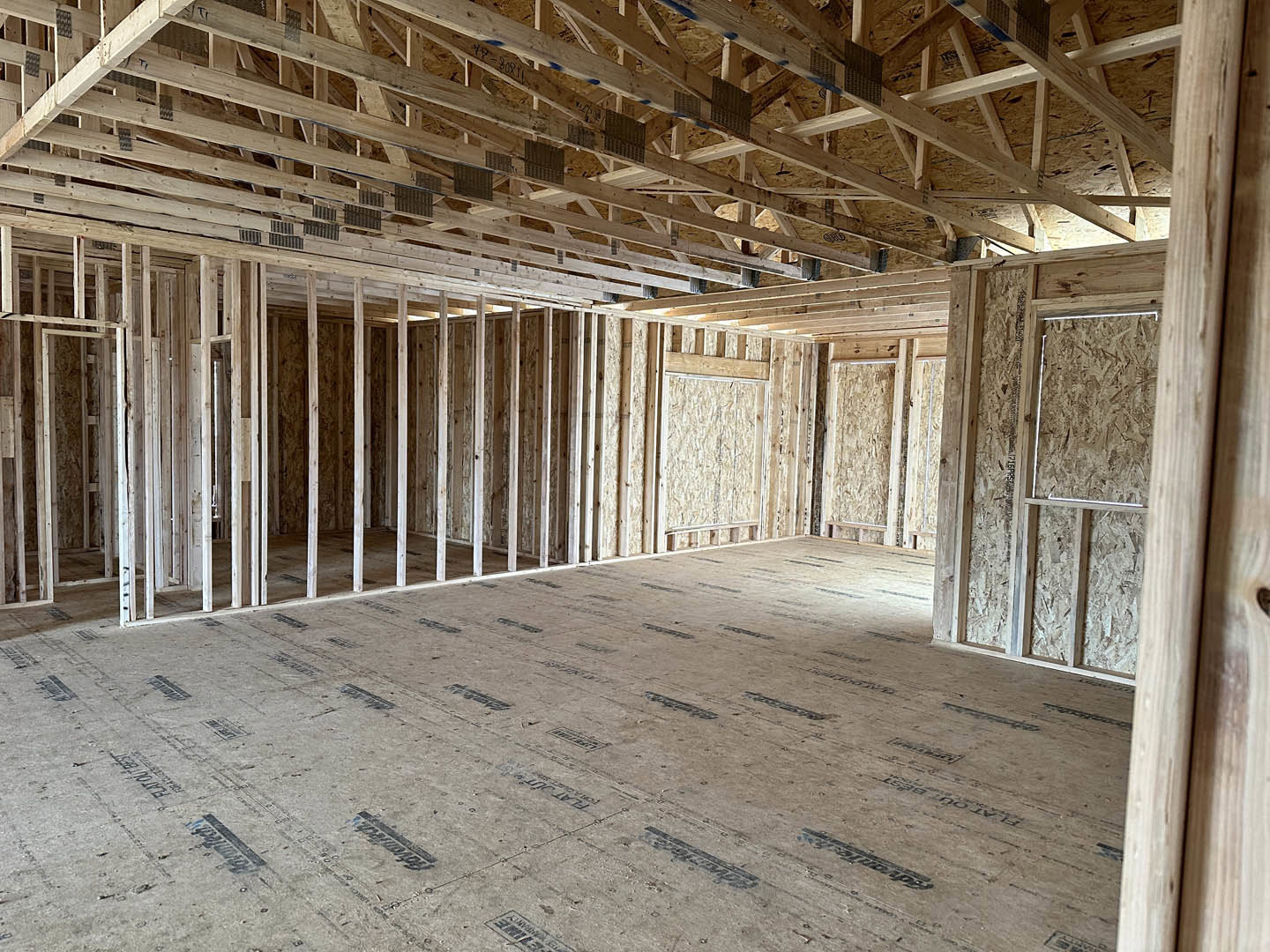Open room with exposed wood ceiling beams, light-colored walls, wooden door, and smooth floor.