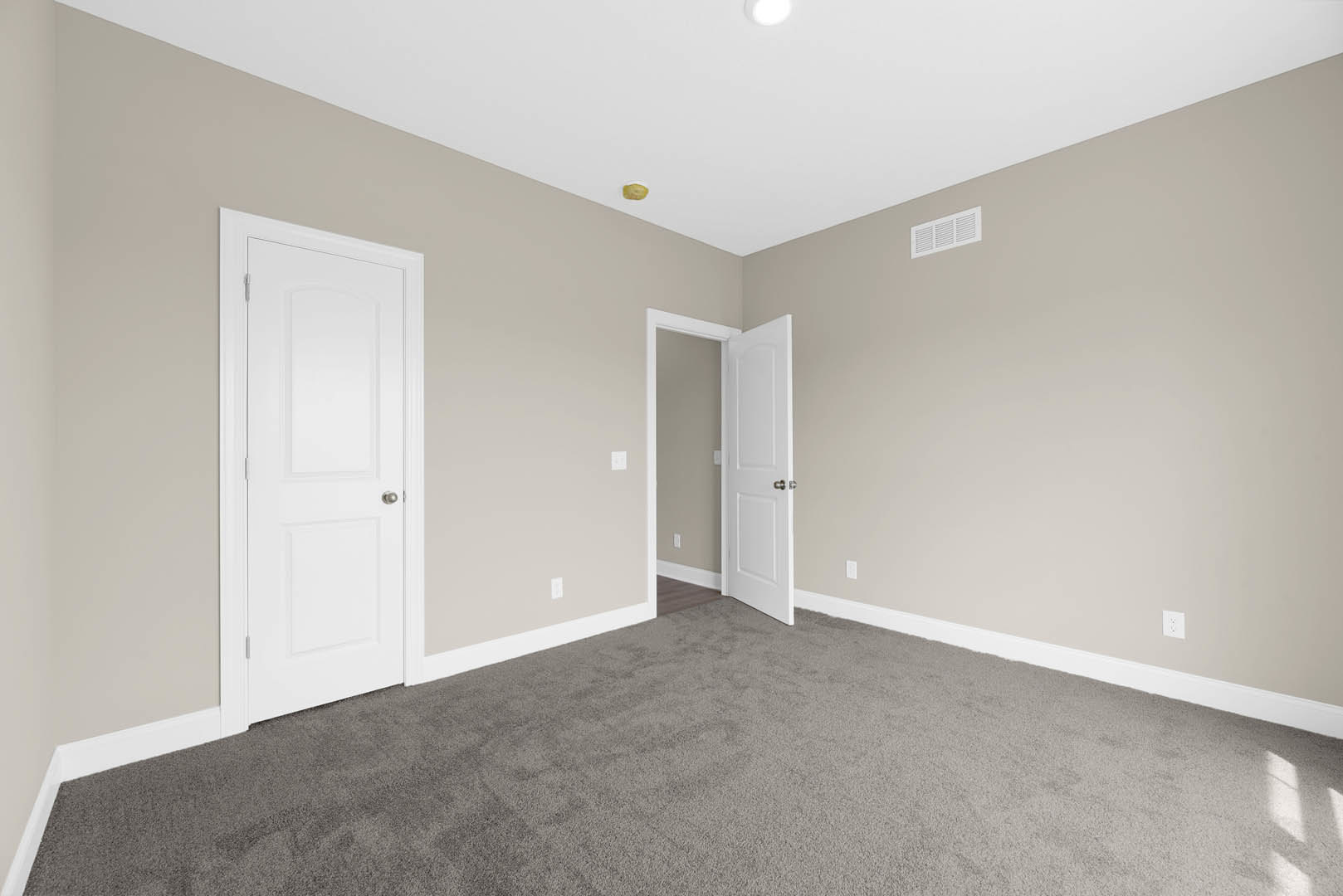 White paneled door with silver knob open to carpeted room, white walls, ceiling vent, and crown molding visible