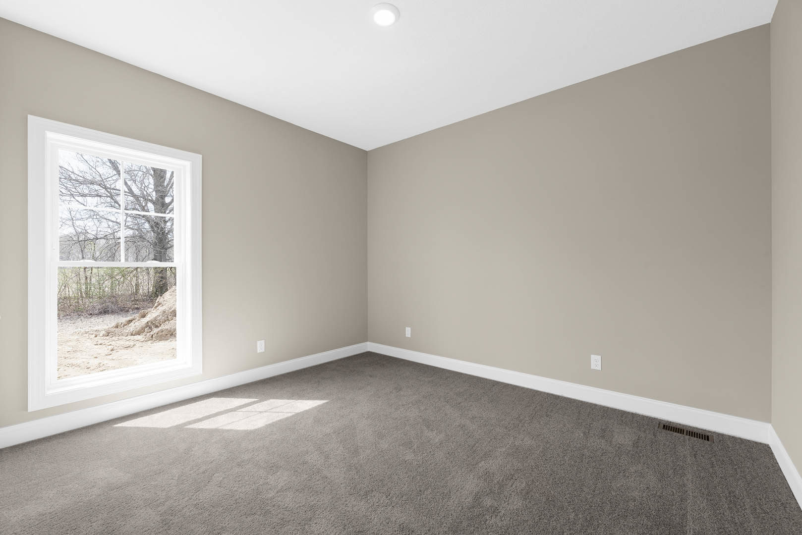 Carpeted room with large window overlooking forest, white walls and ceiling, recessed ceiling light, baseboard molding
