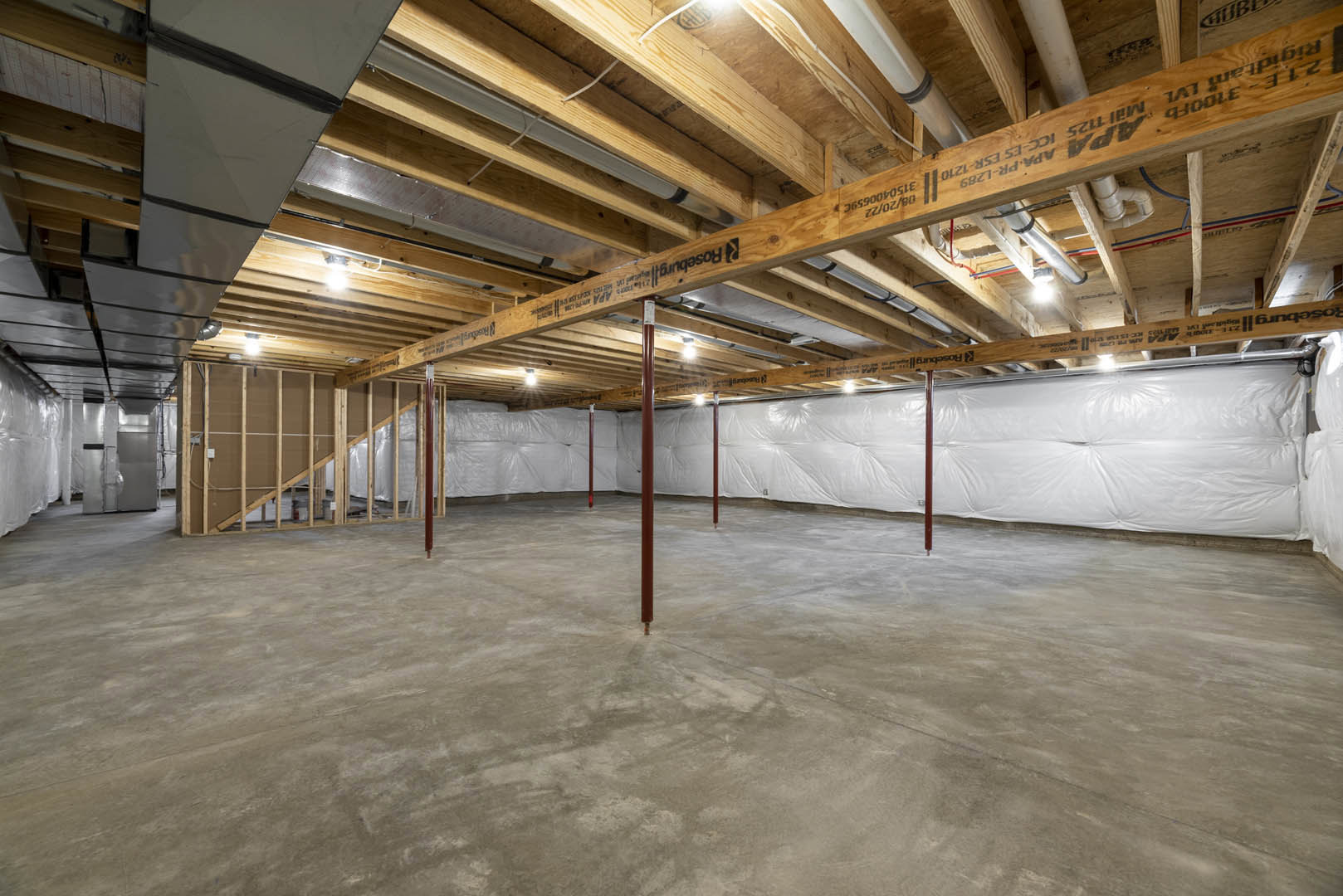 Exposed wooden ceiling beams, white plaster walls, concrete floor with red support pole, unfinished basement interior