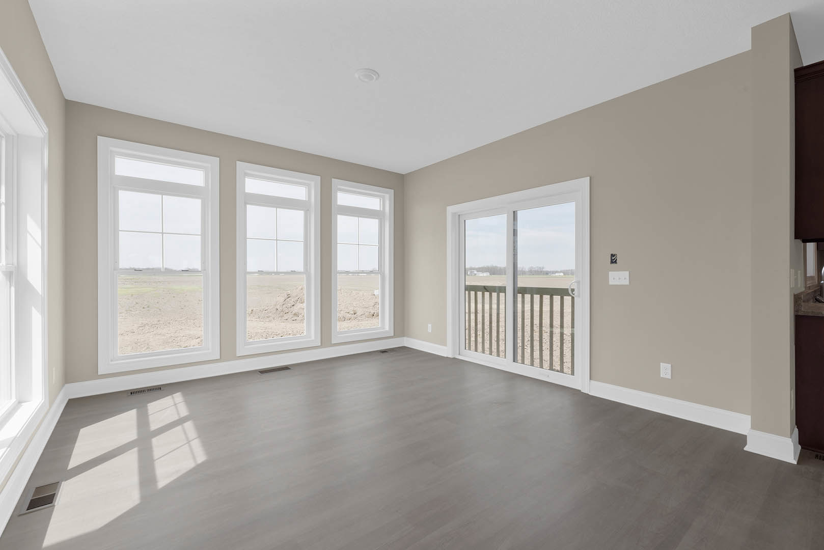 Room with wood flooring, plaster walls, and a row of large windows including a sliding glass door overlooking an open field
