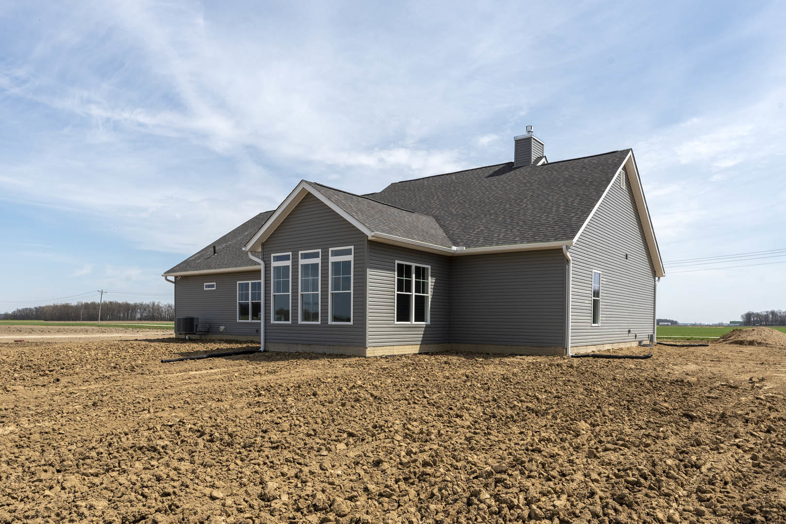 White-framed window and brick chimney on cottage-style house, surrounded by dirt field and sparse grass under cloudy sky