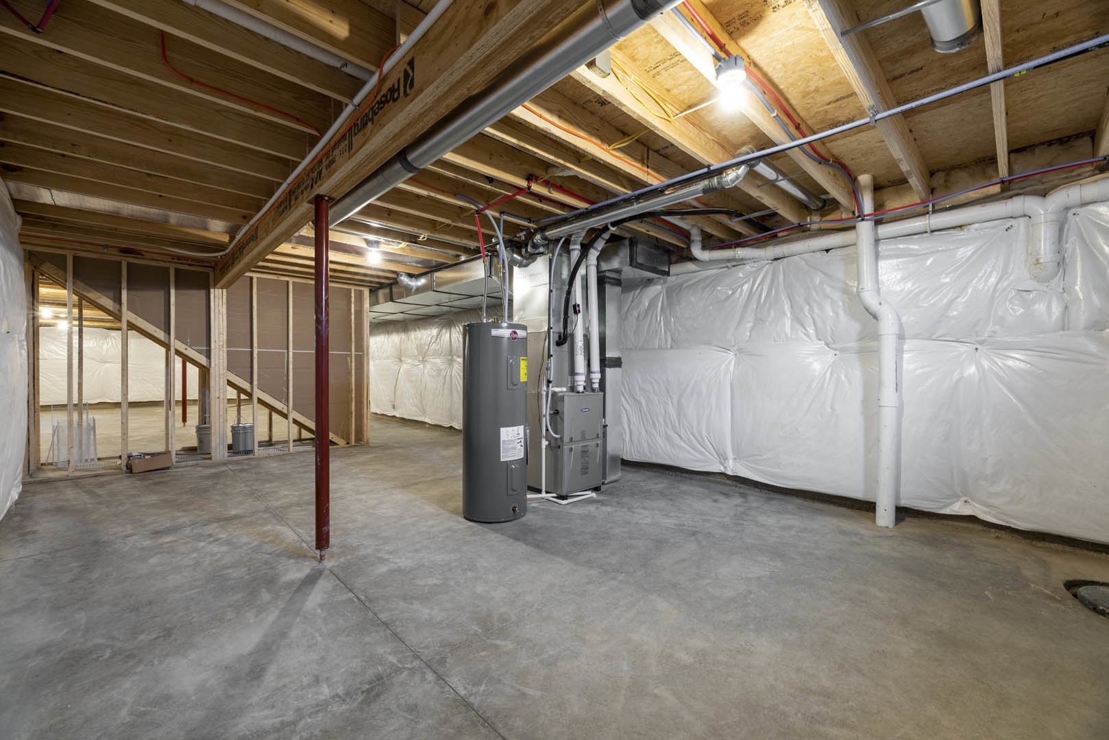 Basement utility room with exposed ceiling pipes, grey metal tank, white sheet insulation, concrete floor, and steel beams.