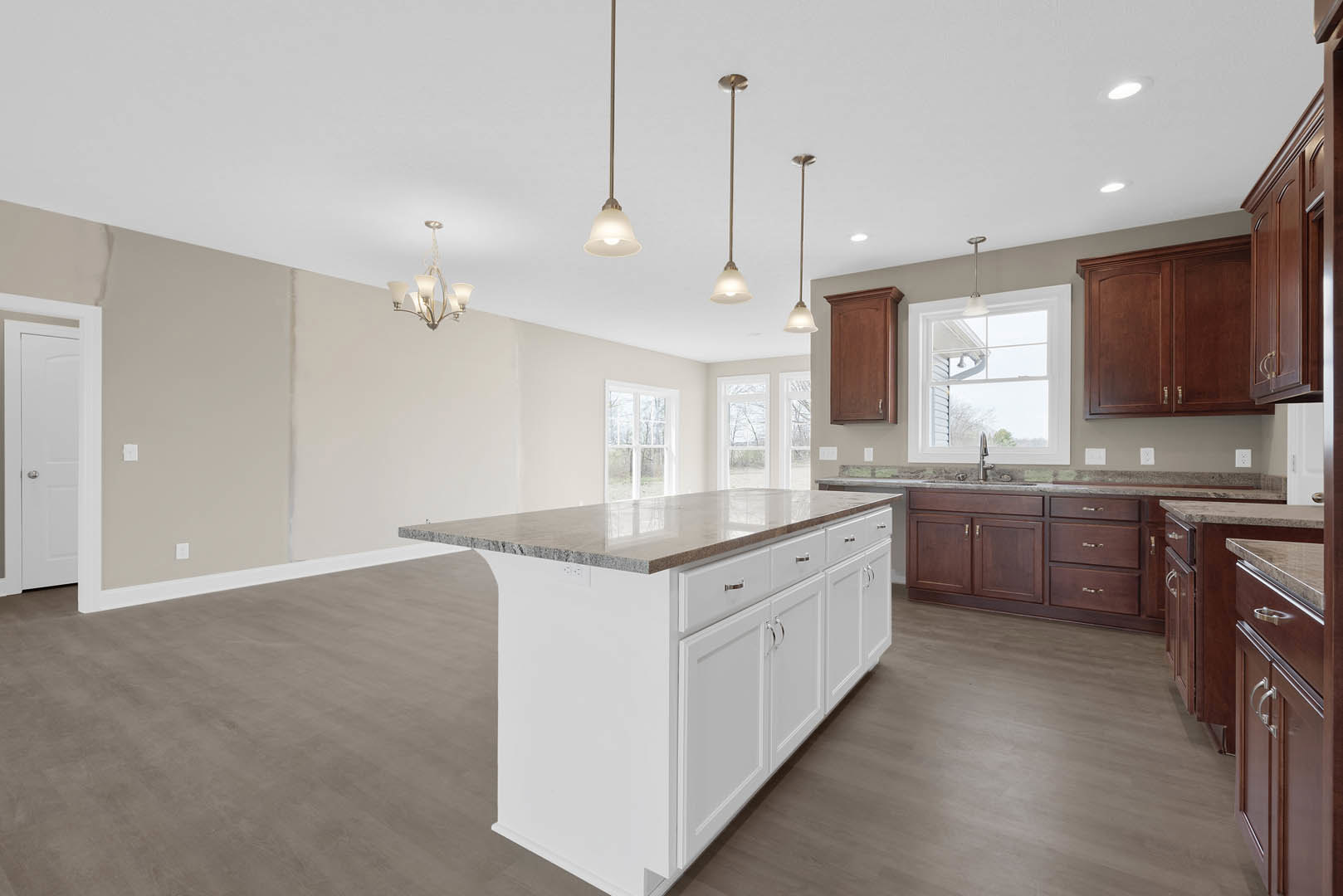 Spacious kitchen featuring a large marble-topped island, white cabinetry, stainless steel sink beneath a row of windows, pendant lights hanging from the ceiling, and a white door