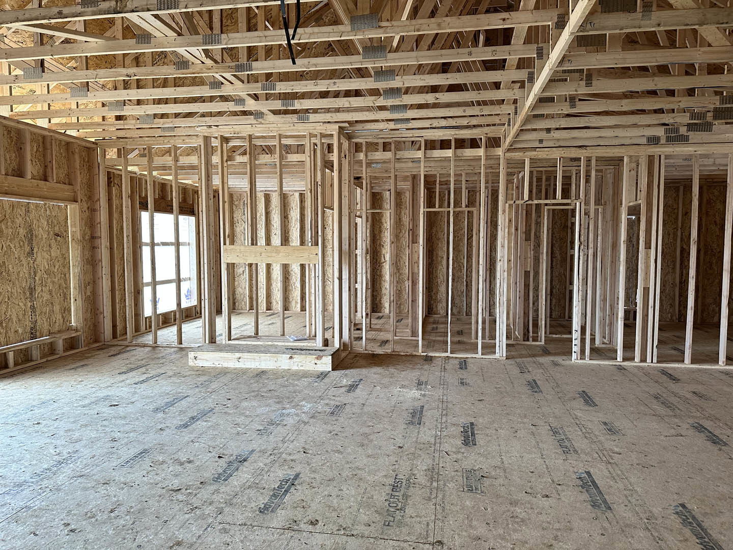 Wood-framed room with exposed beams, unfinished wooden floor, metal roof panels, and a close-up window surrounded by wood planks