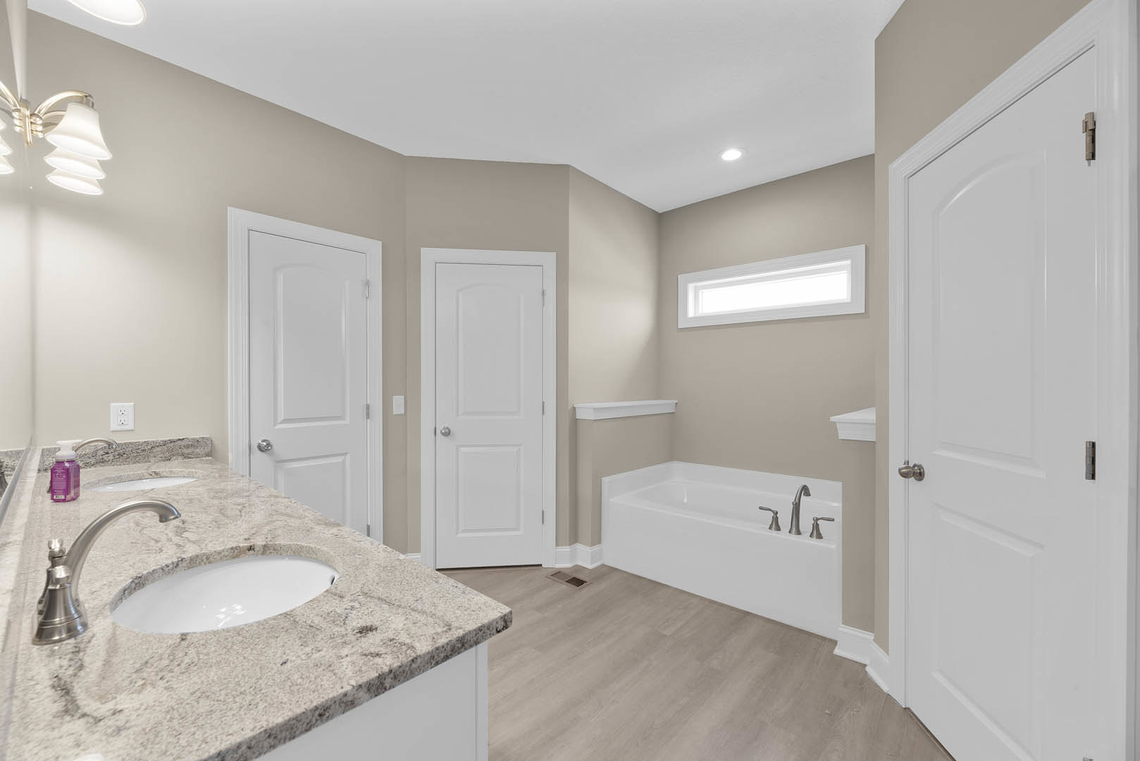 Marble countertop sink with chrome faucet, freestanding bathtub, white cabinetry, silver door knob, purple container with white lid on vanity, tiled walls and floor