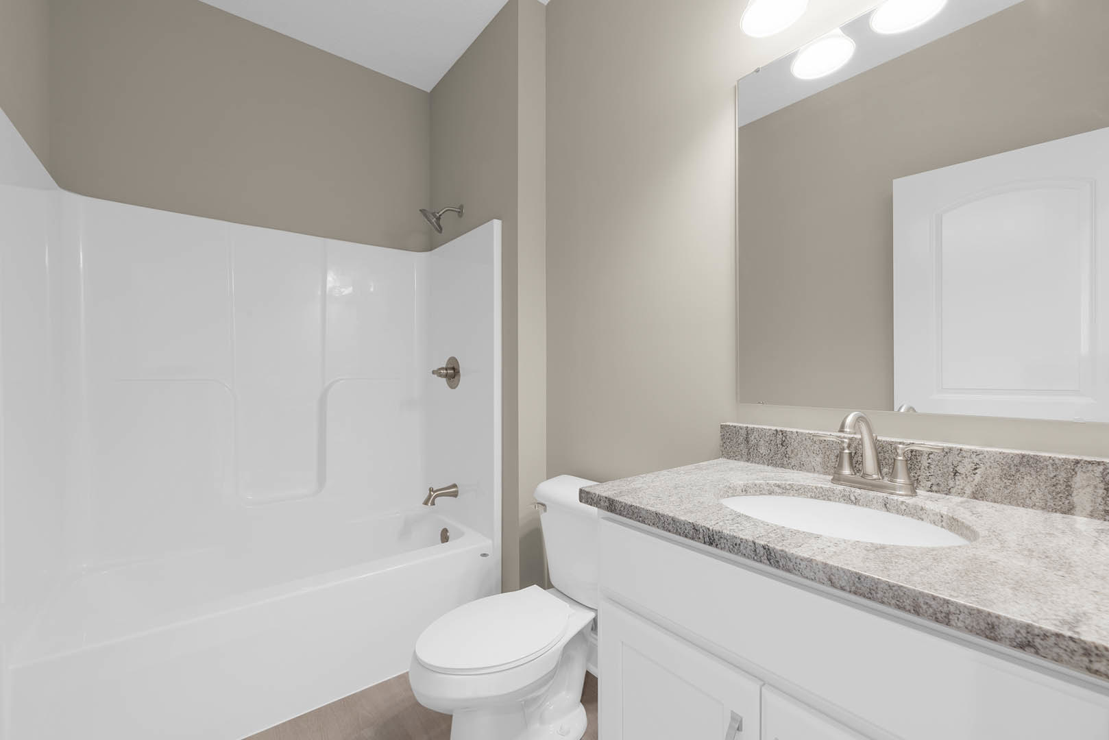 Bathroom with white tile walls, white bathtub, curved shower head, white toilet with closed lid, and close-up of sink beneath a wall-mounted light.