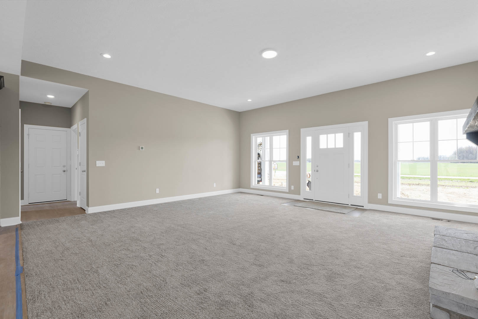 Beige carpeted room with white paneled doors, silver handles, large window overlooking a grassy field, white walls and ceiling