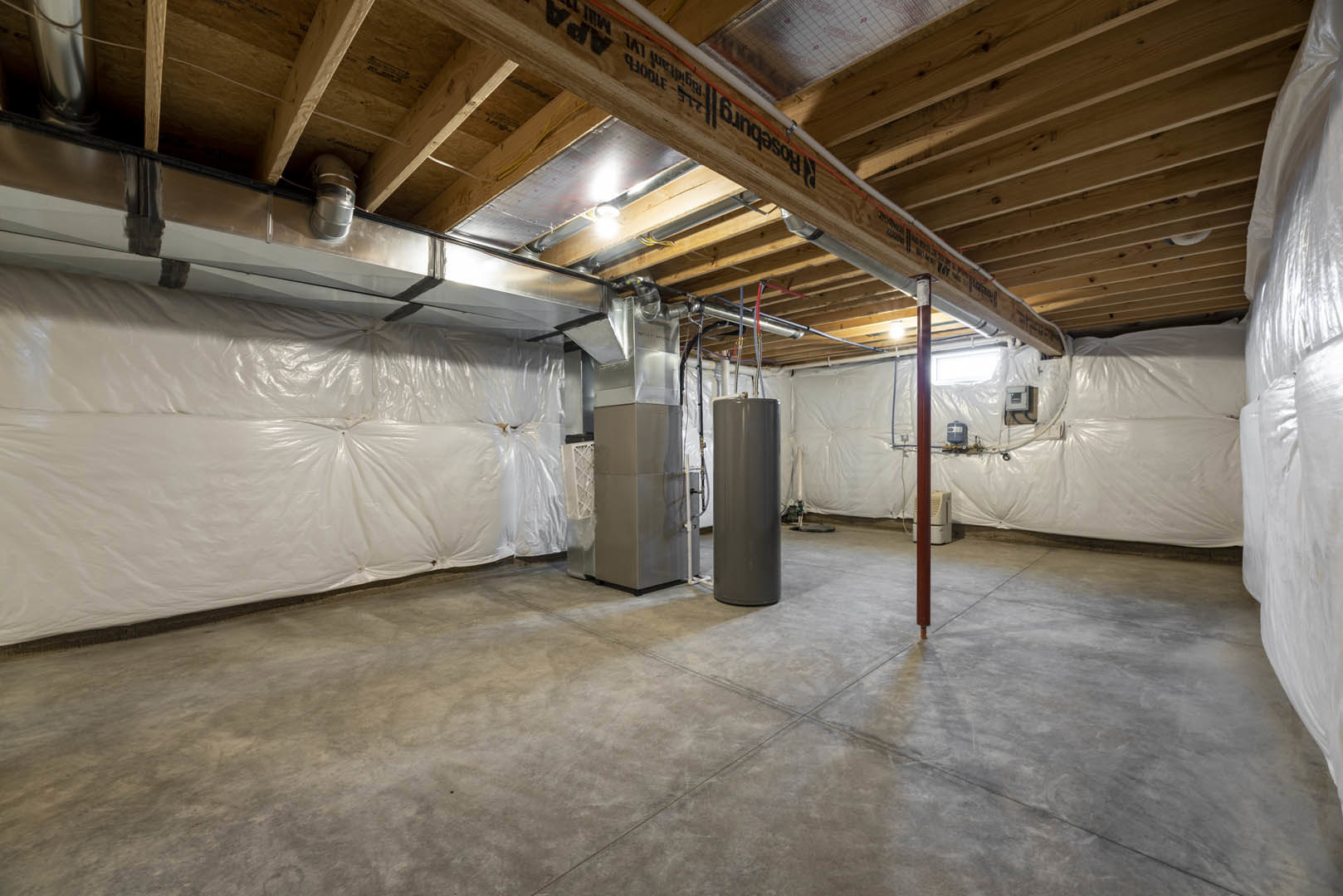 Concrete floor and plaster walls in a basement room featuring a grey metal cylinder, exposed wood beam with black text, and a metal pole near the corner.