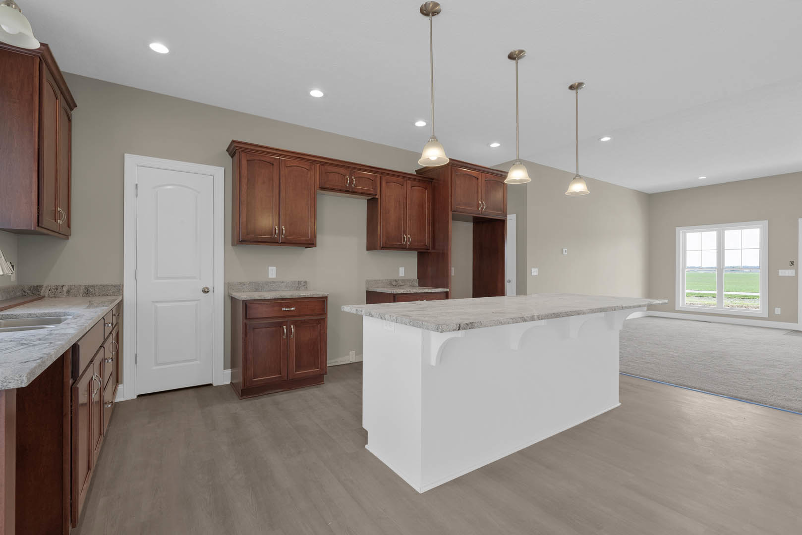White kitchen with marble-topped bar, shaker cabinets, stainless hardware, window overlooking lawn, and light wood flooring.