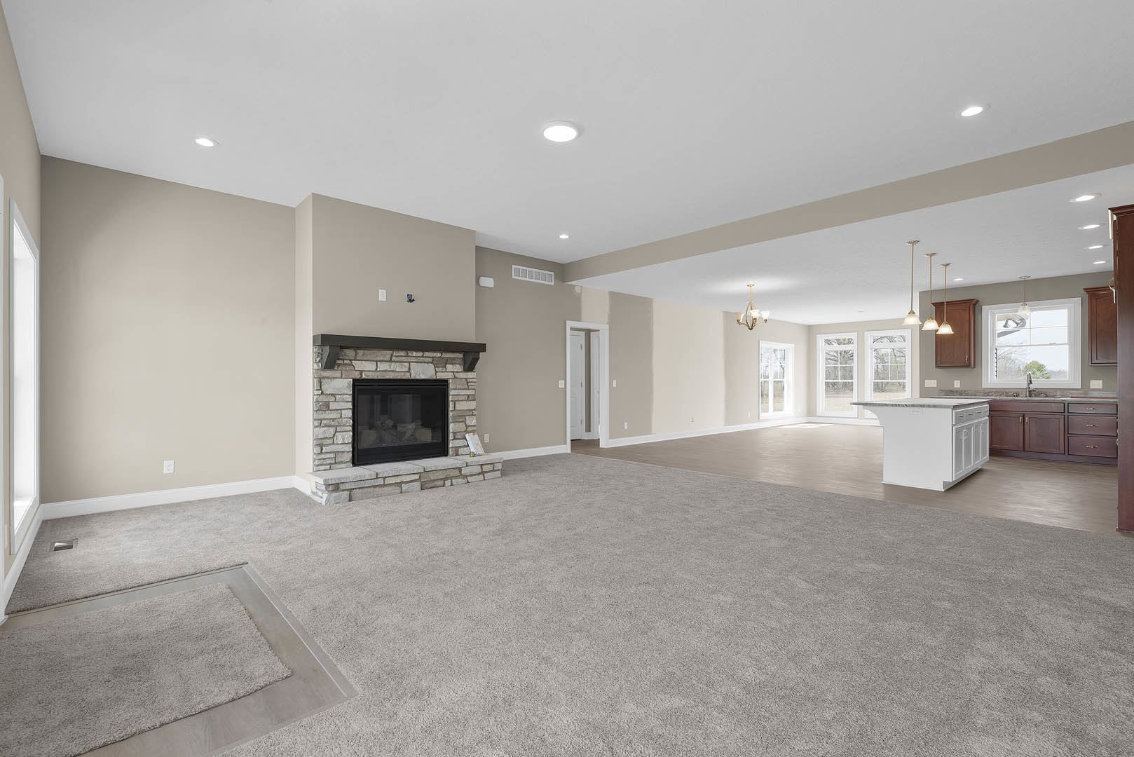 Open living room with light carpet, black-framed glass fireplace, and adjacent white kitchen island with drawers, white cabinetry, plaster walls, and ceiling.