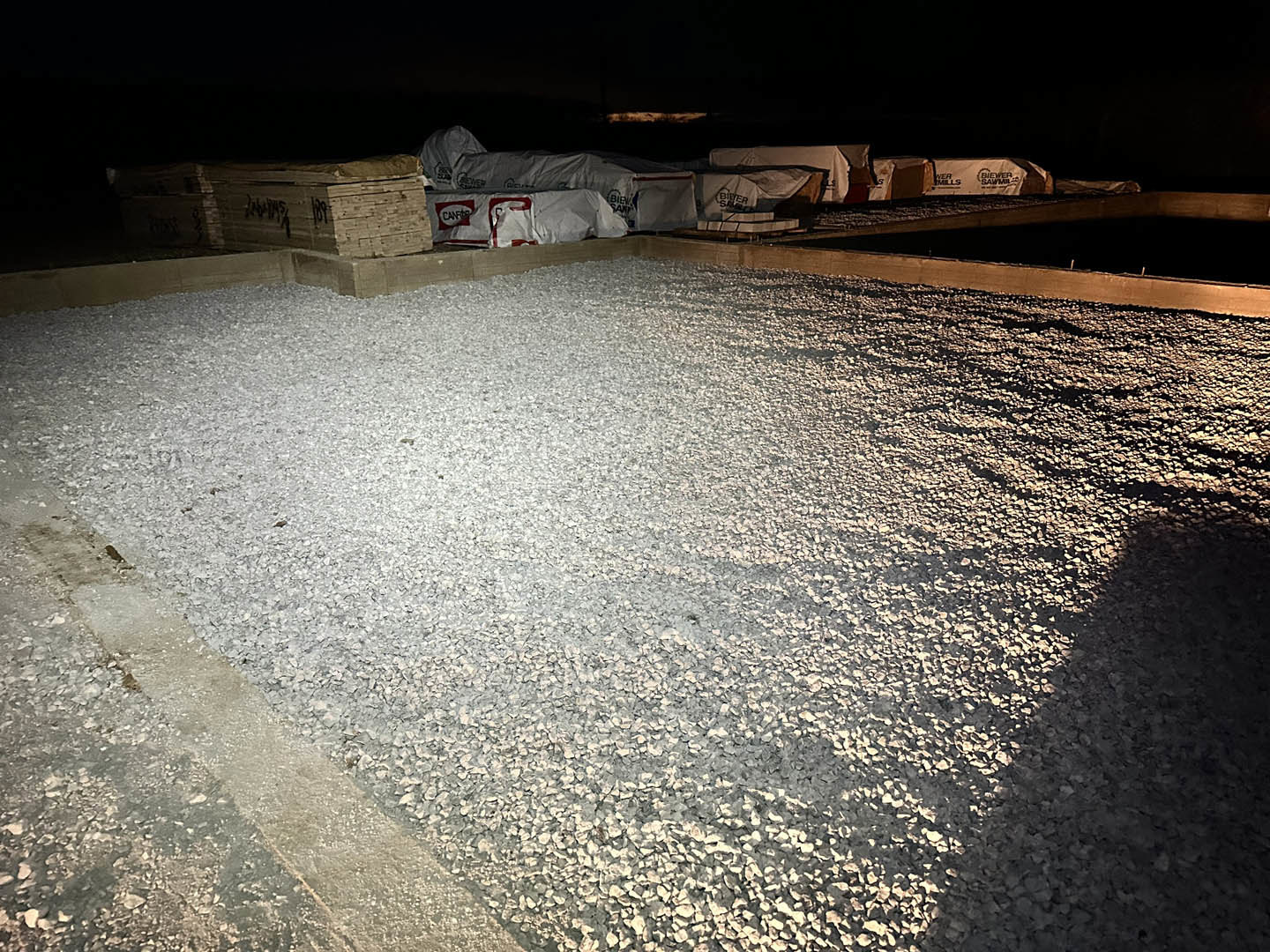 White gravel piled on a smooth concrete patio, with a white and red bag and a sign featuring black text nearby.