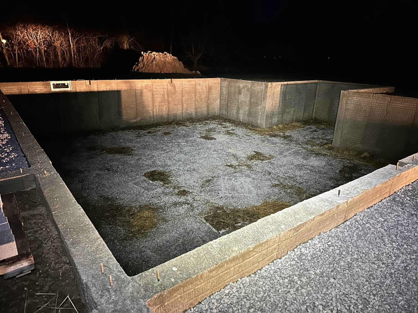 Square concrete foundation with concrete walls, gravel border, bare trees in background, and close-up views of stone and brown materials.