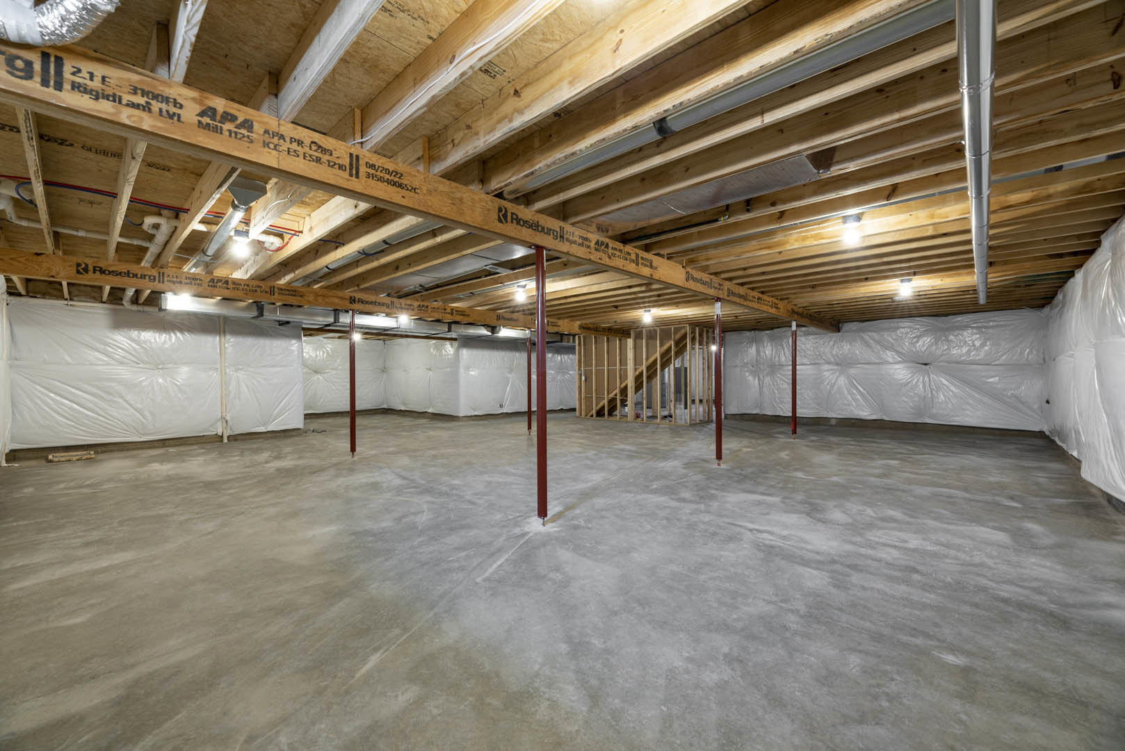 Exposed wooden ceiling beams, concrete floor, white walls, stack of white bags, metal pole, unfinished basement interior