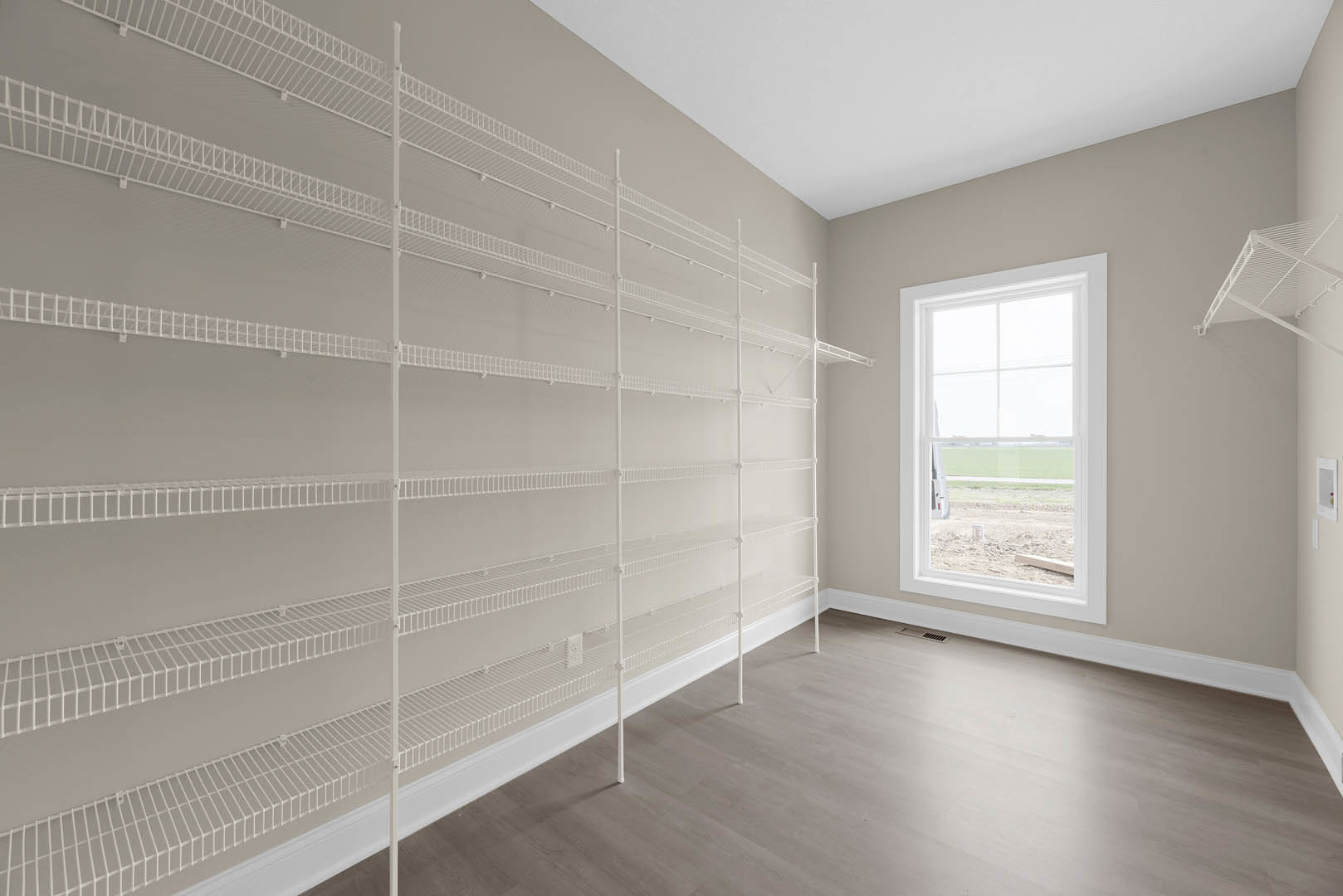 Built-in white shelves along a plaster wall, large window overlooking grassy field, light wood flooring, white railing visible in foreground