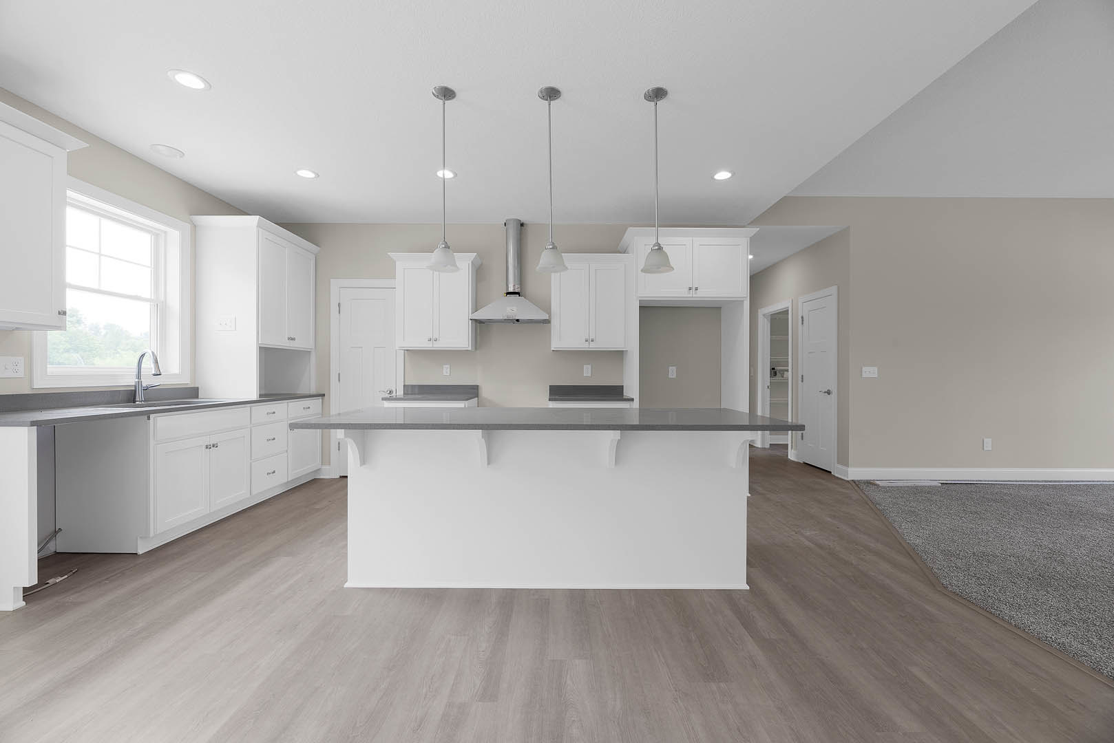 Spacious kitchen featuring a large central island with white countertops, stainless steel faucet, white cabinetry, and modern appliances against a white wall