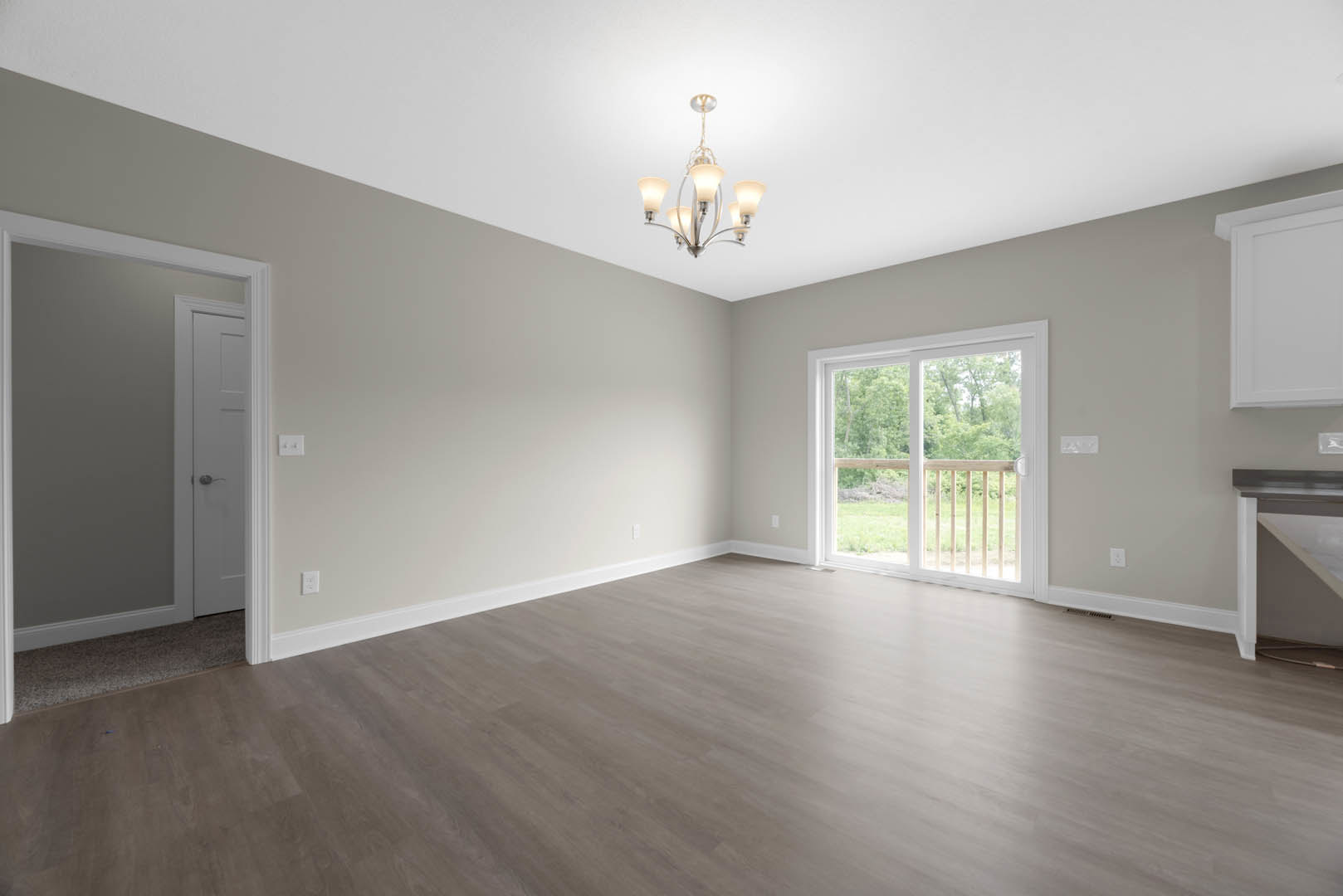 Chandelier hanging above wood laminate flooring, white walls with crown molding, sliding glass door framed by wooden railing, white interior door with silver doorknob