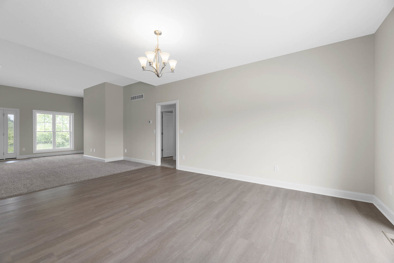 Chandelier with five lights hanging from ceiling, hardwood floor, white door with black handle, large window showing trees outside, plaster walls