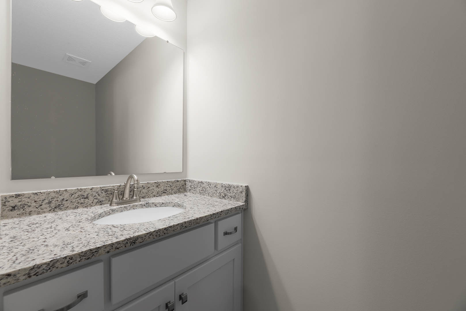 Marble bathroom countertop with undermount sink, chrome faucet, white cabinetry, wall mirror, and overhead lighting fixture