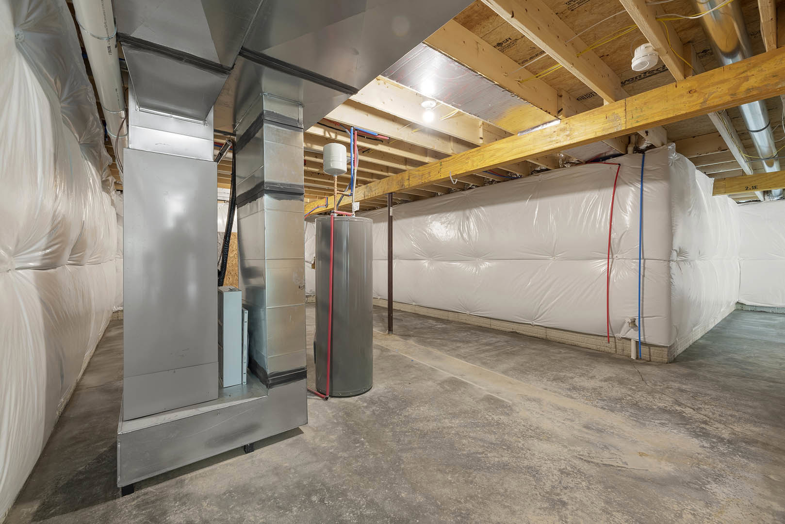 Basement room with exposed wood beams, concrete walls, large grey metal tank, white cylinder on shelf, white plastic bag hanging, and white board casting shadow.
