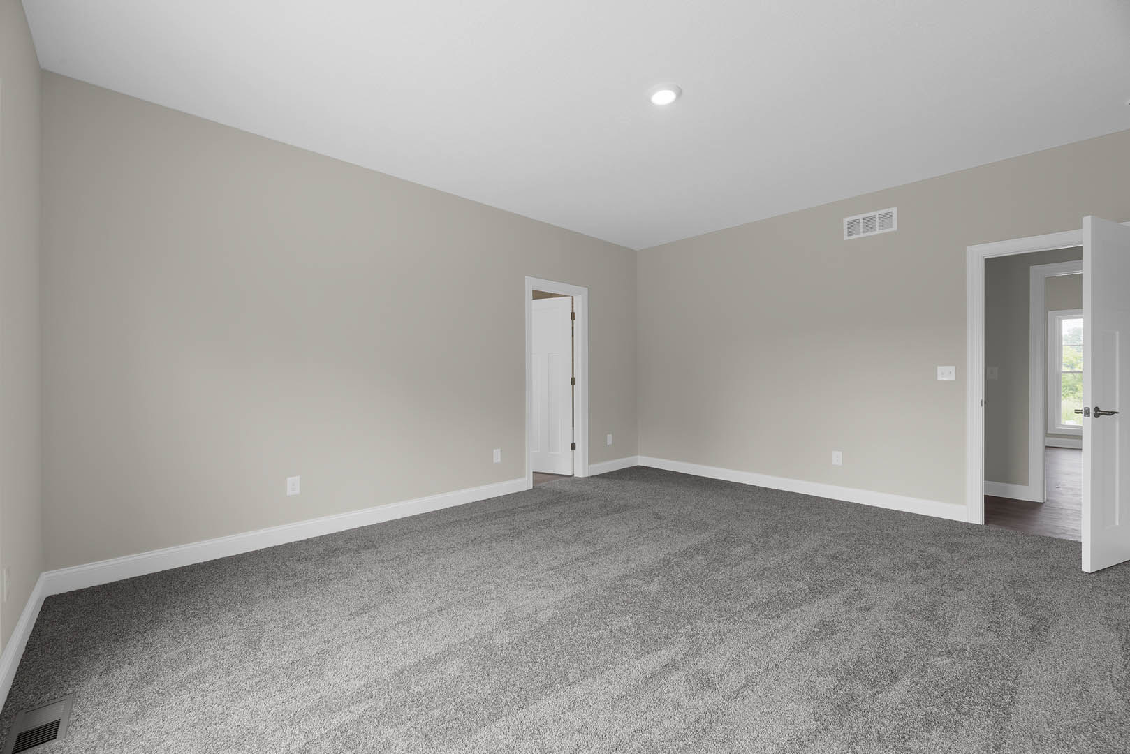 White carpeted room with open white door, wall vent, and window visible through doorway