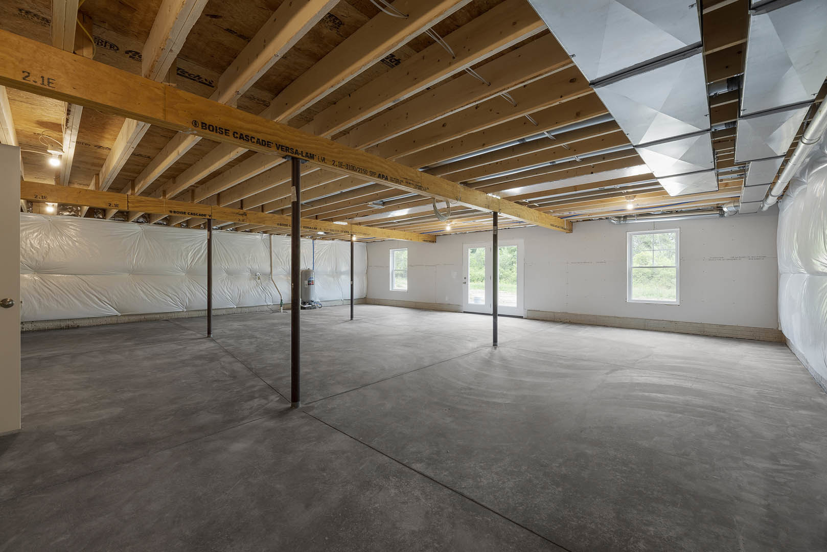 Wooden ceiling with exposed wood beams, concrete floor with metal support poles, white-framed window, metal ceiling panels, white tarp covering one wall, unfinished and empty
