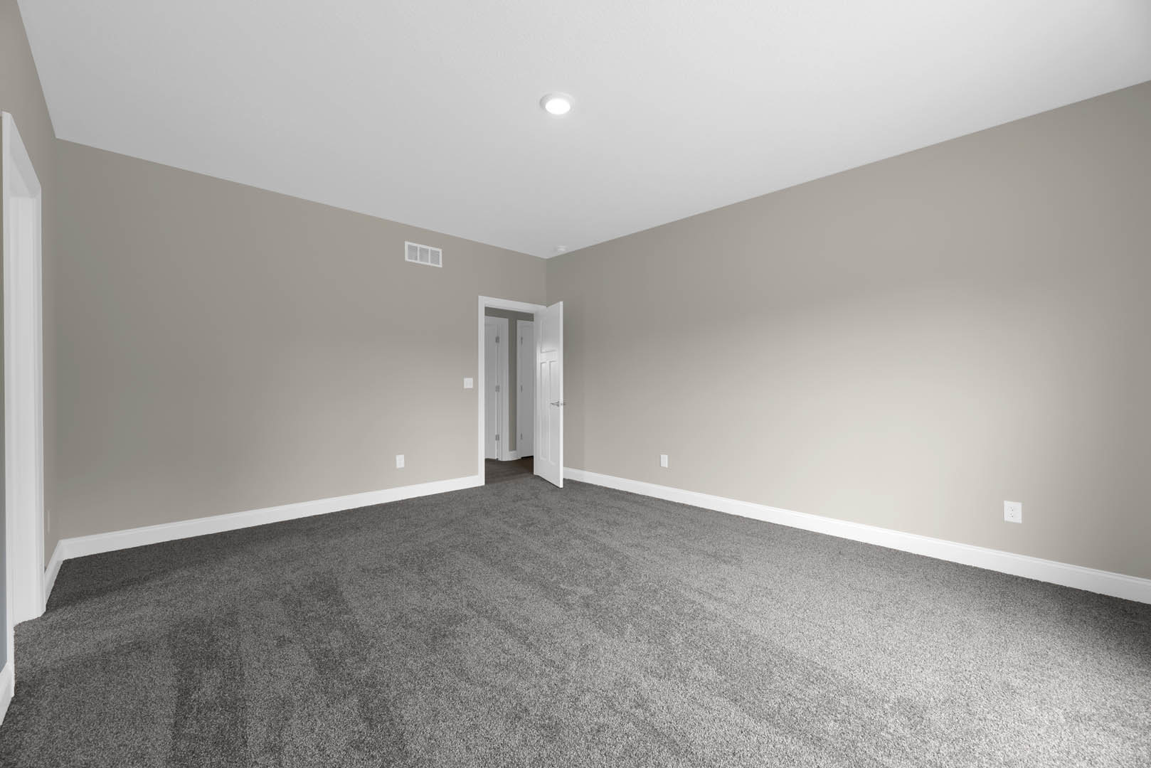 White interior room with grey carpet, open white door, white walls featuring black trim, and ceiling light fixture
