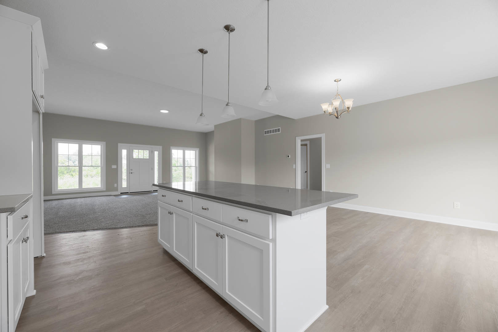 White kitchen island with shaker cabinets and drawers, quartz countertop, stainless steel sink, pendant chandelier overhead, white walls with black trim, glass-paneled door