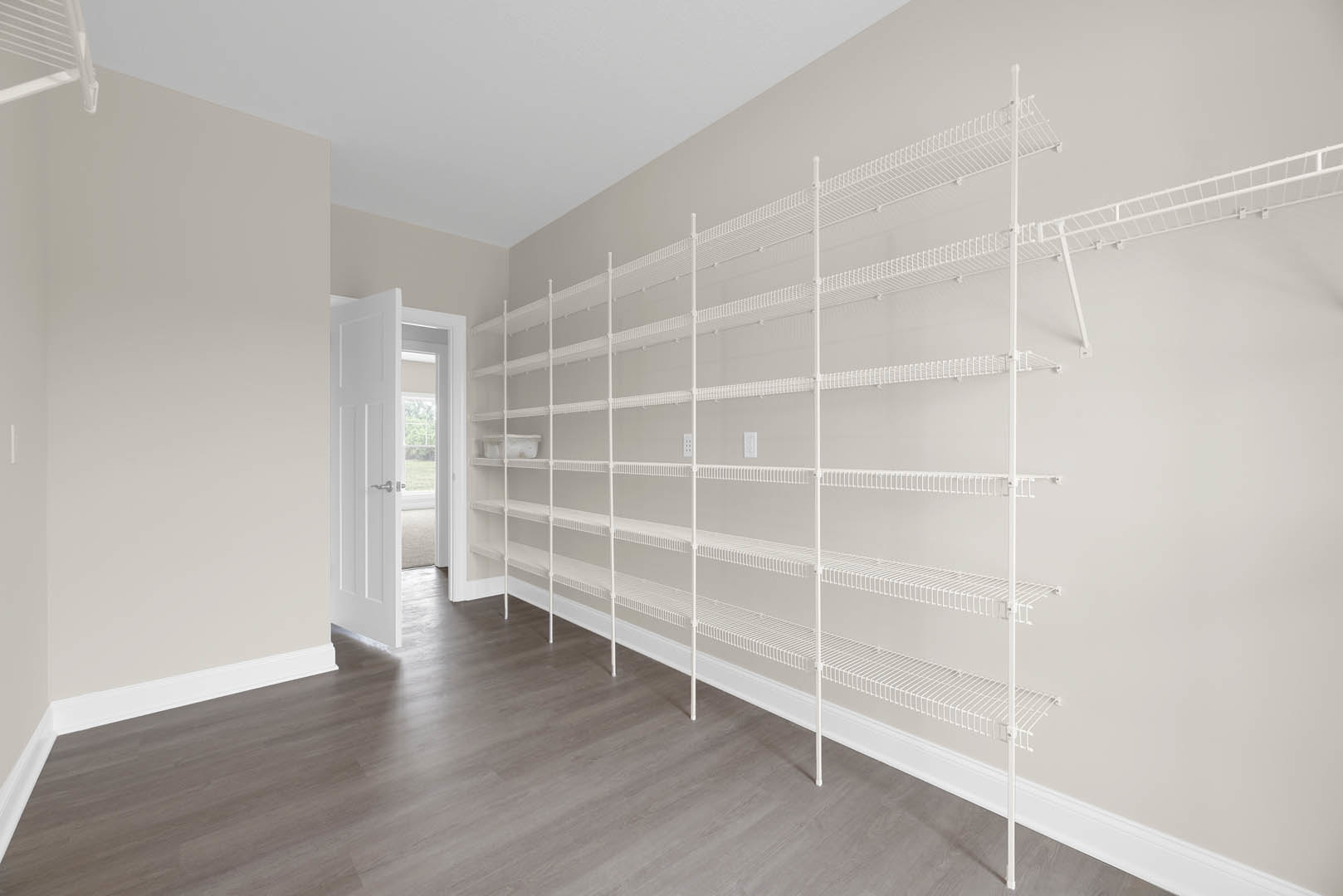 White built-in shelves against a plaster wall, wooden floor, white door with silver handle, window overlooking grassy field, close-up of white staircase railing.