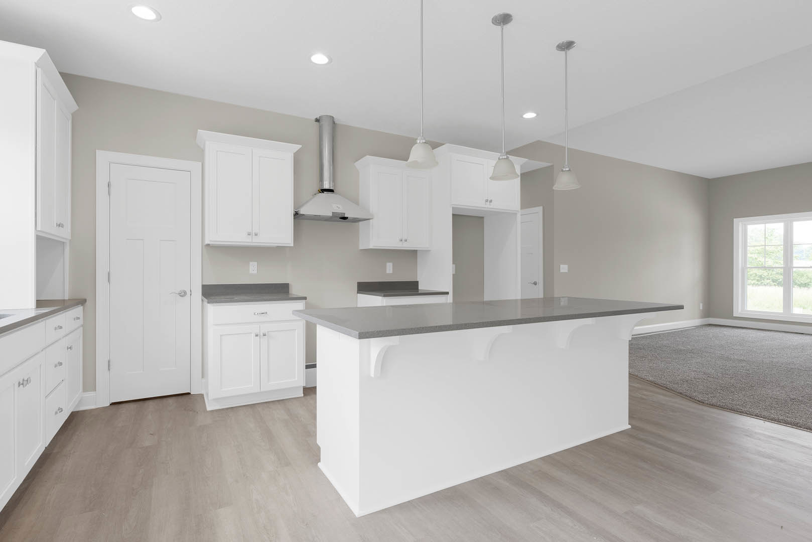 Kitchen with white shaker cabinets, white quartz countertop bar, stainless steel sink, wood plank flooring, silver hardware, window overlooking outdoors, white interior door