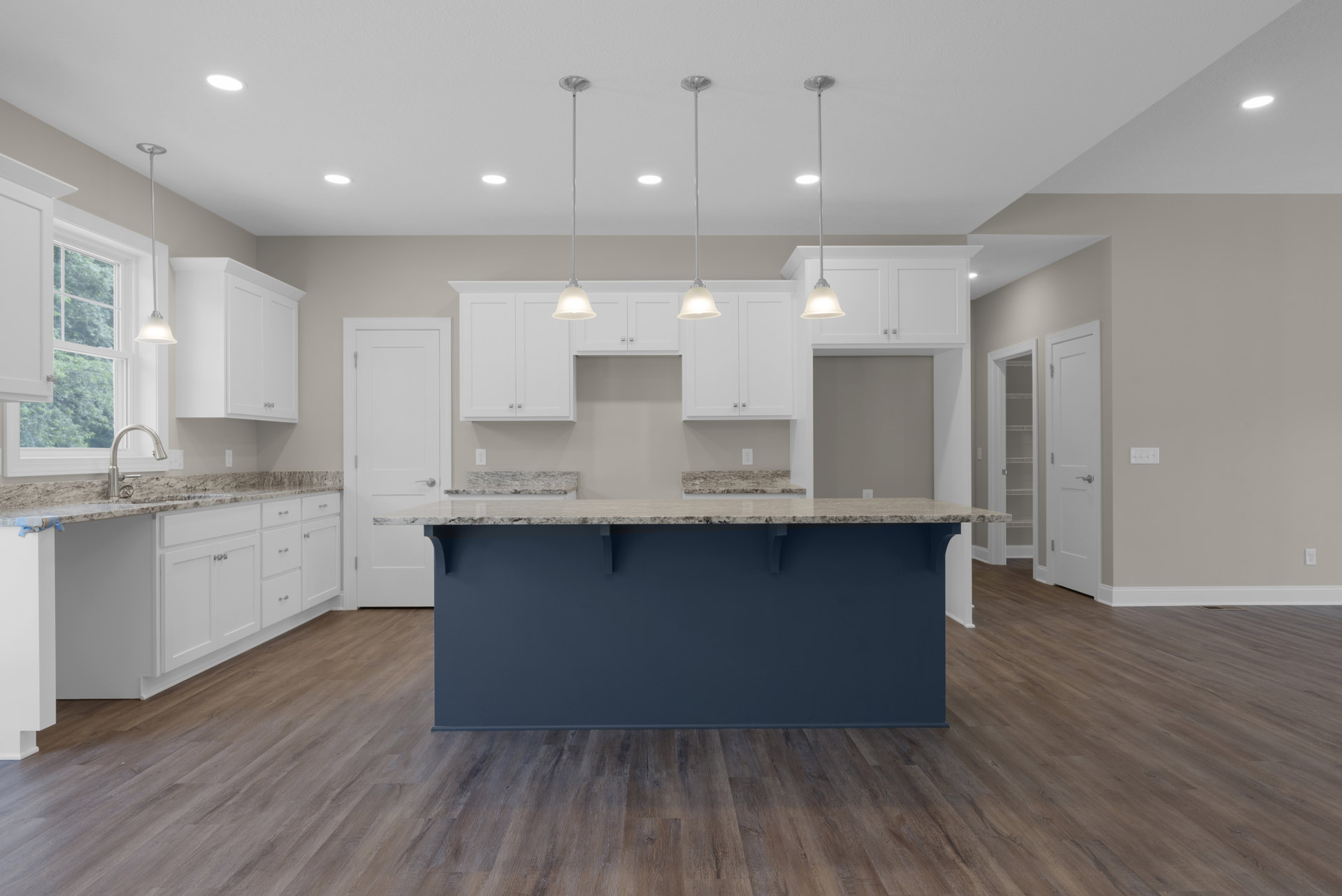 Kitchen with white shaker cabinets, central island, wood flooring, blue accent wall, pendant light fixture, white door with silver handle, and tiled backsplash.