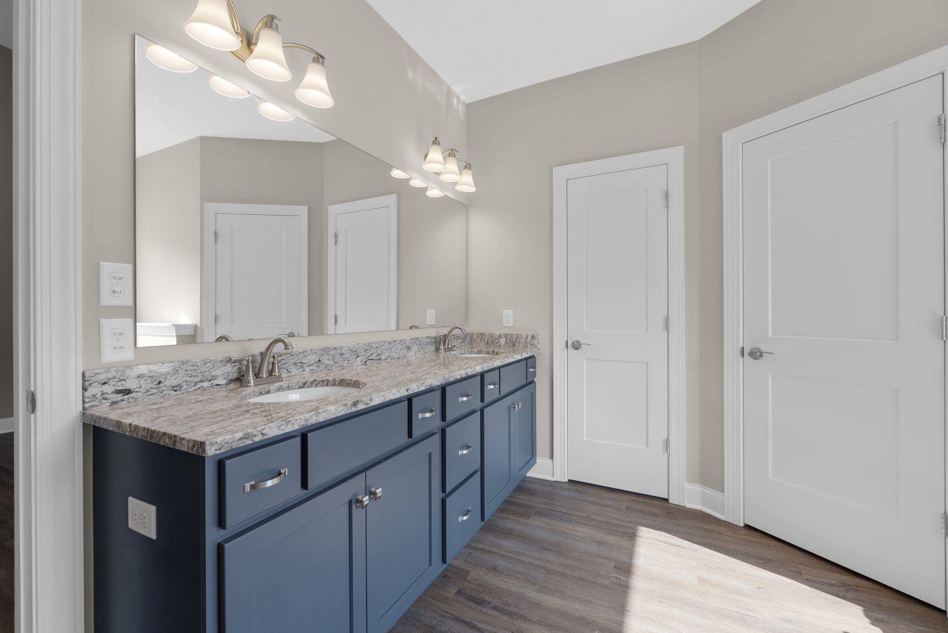 Bathroom featuring marble countertop with double sinks, white cabinetry, silver faucet fixtures, white door with silver handle, light fixture and light switch on tiled wall