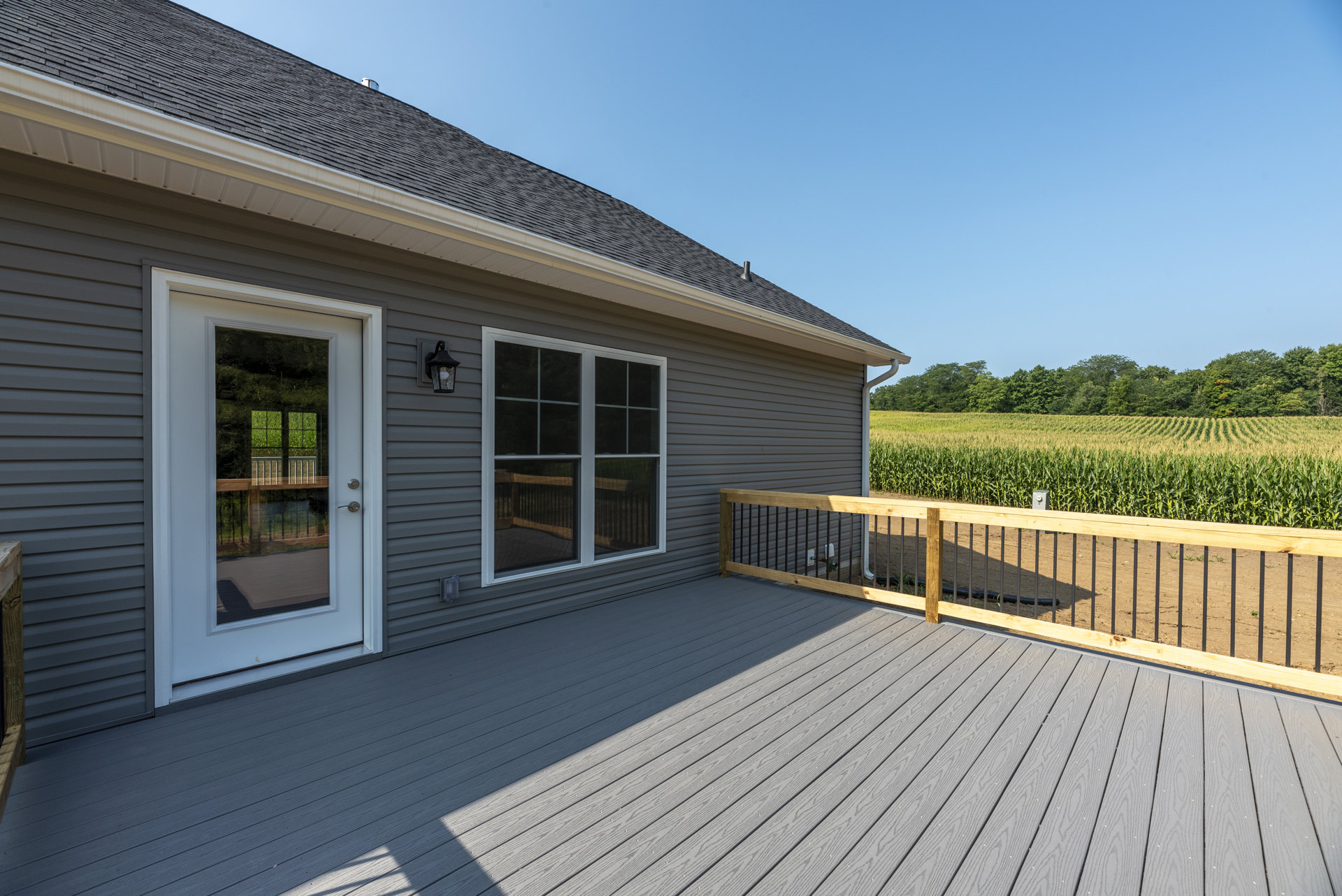 Wooden deck with railing, glass door, and window overlooking a corn field