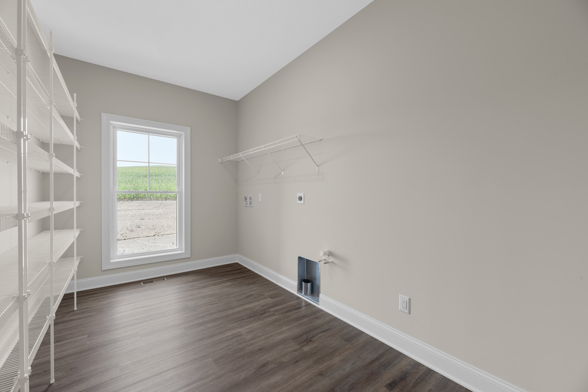 Wood flooring room with white wall shelves, large window overlooking grassy field, silver metal trash can in corner