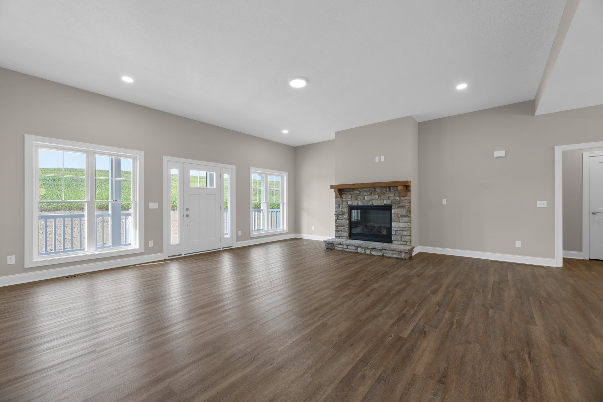 Living room with hardwood floor, fireplace featuring a wood mantel and glass door, white door with glass panes, large window overlooking a grassy field, plaster walls and ceiling.