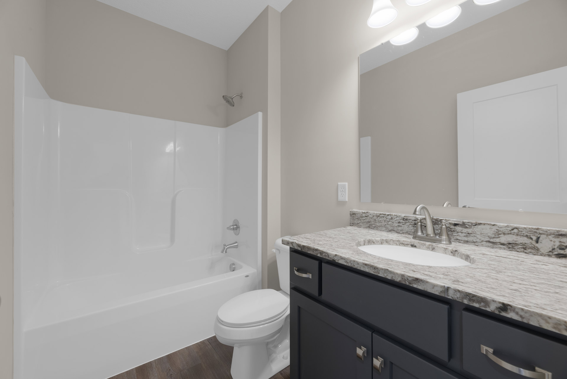 Bathroom with white bathtub, toilet, and sink set in light-colored cabinetry; tiled walls and floor, white door, wall-mounted light fixture.