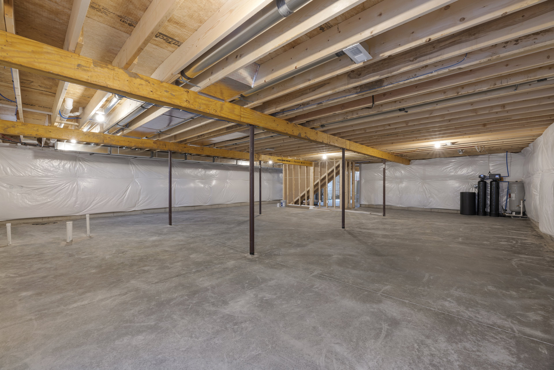 Wooden ceiling with exposed beam, concrete floor with metal poles, visible pipes and white vent on shelving along unfinished walls.