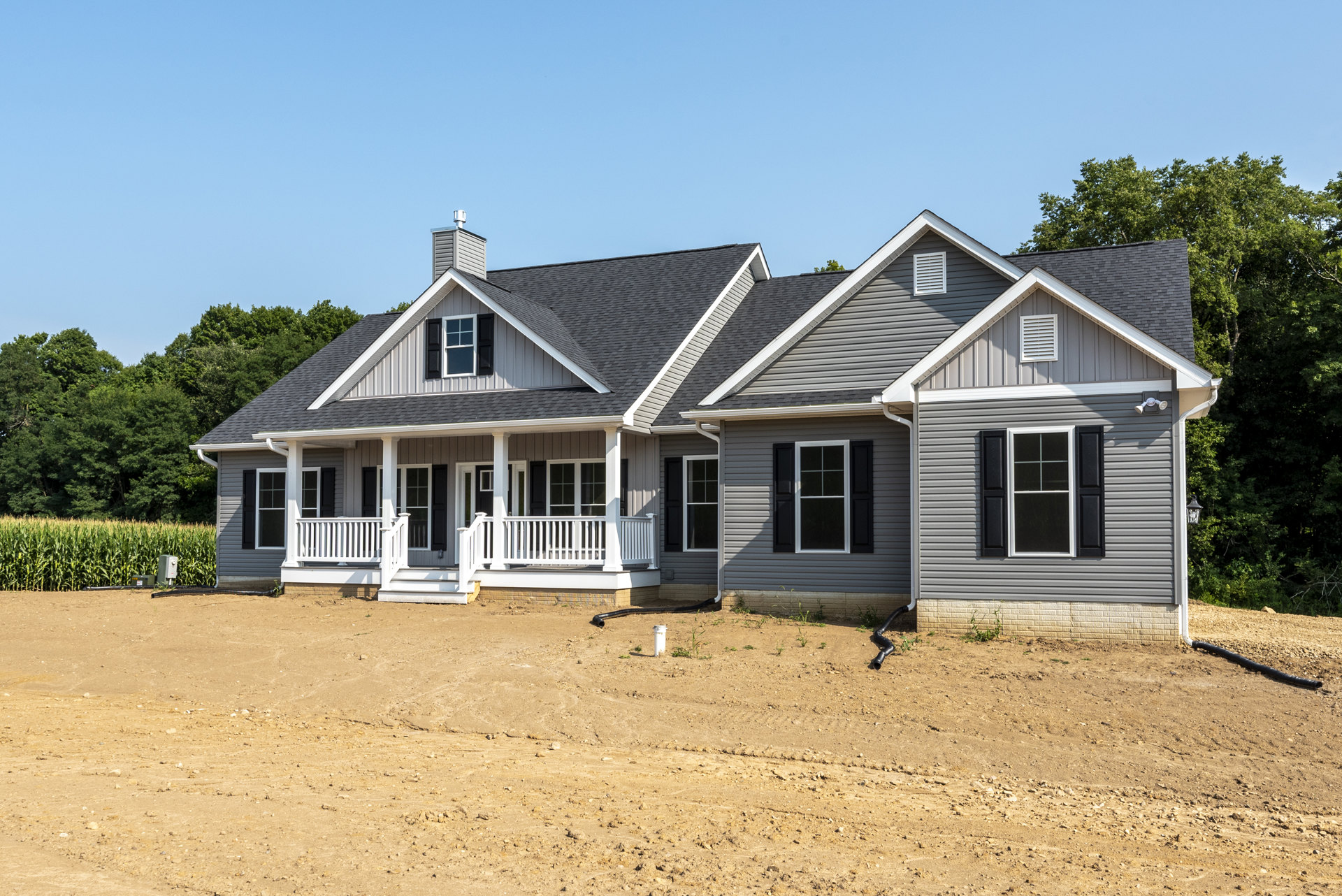Two-story house with grey siding, white trim, black shuttered windows, white vent, covered porch, and dirt yard in front