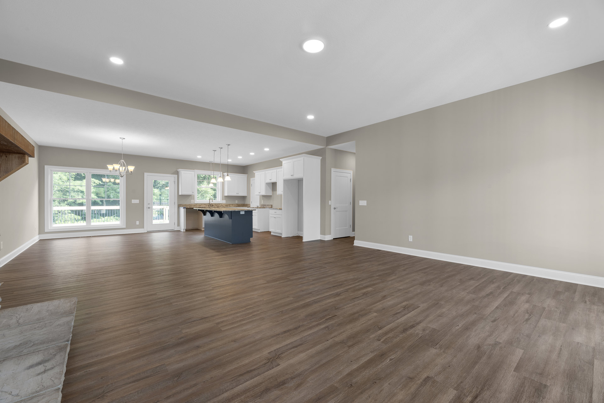 Spacious room with wood flooring, pool table centered beneath ceiling light, white door with silver handle, large window overlooking trees, exposed wood beam detail