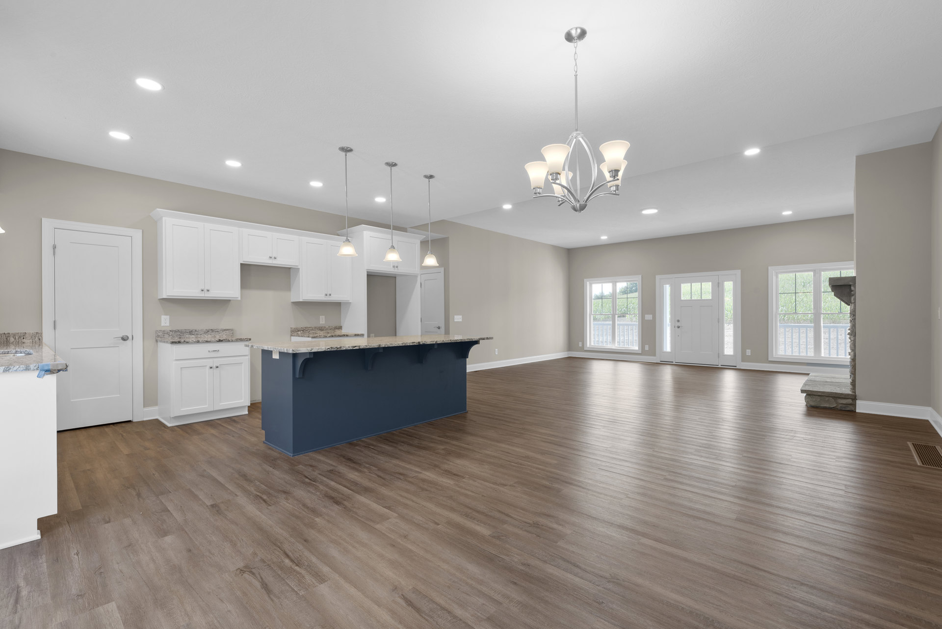 Open-concept kitchen with white cabinetry, central island featuring stone countertop, hardwood flooring, white walls, stainless steel appliances, and a white door with glass panels