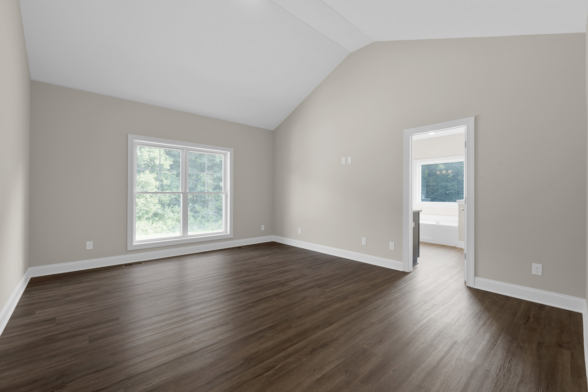 Room with hardwood floor, white walls, white ceiling, large window showing trees outside, sunlight reflecting on floor