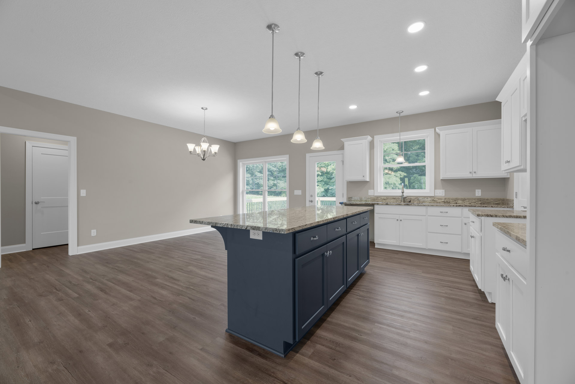Kitchen with wood flooring, central island featuring marble countertop, white cabinetry, stainless steel sink, modern light fixture, and white door with silver handle